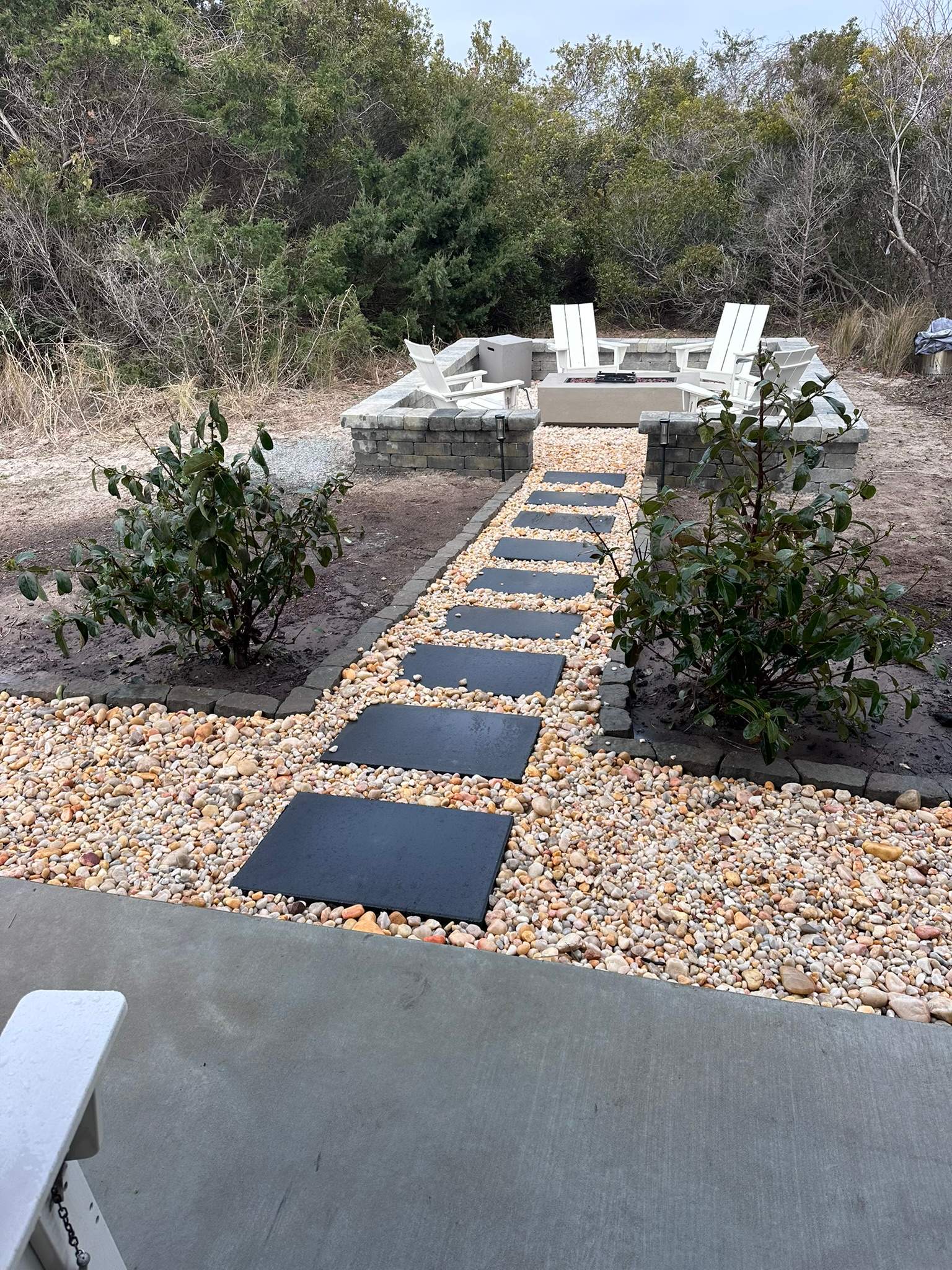 Backyard stone walkway leading through river rock to a fire pit seating area